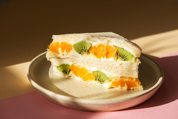 Half sandwiches bread stuffed with mascarpone cream cheese, kiwi and orange in a plate. Homemade Korean dessert. Hard light.
