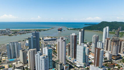 Panoramic photograph of the city of Itajaí and its Itajaí-Açu River flowing into the sea, with a ship maneuvering.