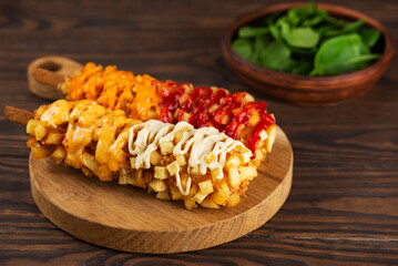 Corn dogs with sausage, cheese, potatoes and sauces on a wooden board with spinach. Korean street food.
