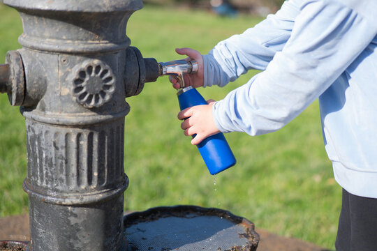 Child Filling Water Bottle at Outdoor Fountain in Park