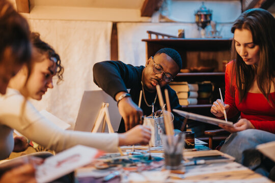 A diverse group of friends participates in a creative painting session, enjoying quality time together while working on their individual art projects indoors in a cozy and inspiring environment.