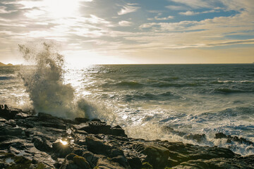 Ocean waves crashing against rocks under a vibrant sky