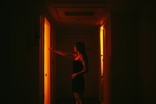 Woman opening a glowing hotel room door at night