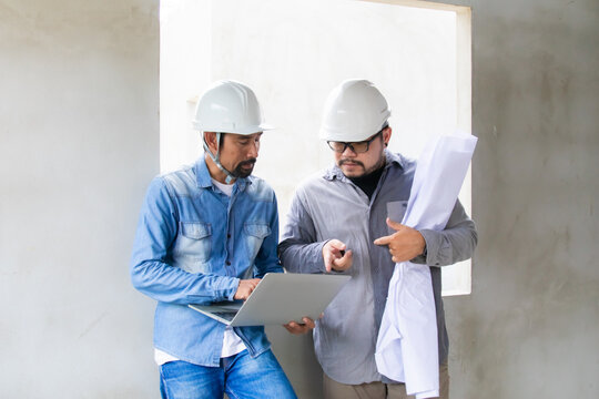Portrait of two engineers or architects male, with safety helmets and laptop, collaborating on-site, reviewing digital blueprints and discussing the next steps in the construction project, men at work