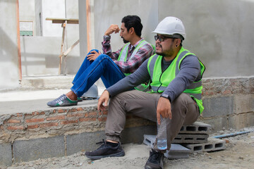 Two Asian builder workers wearing safety reflected vest and helmet tired thirsty hydrated drinking...