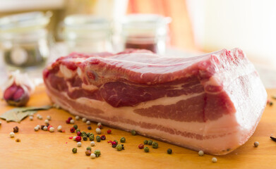 Fresh piece of pork belly on wooden board with spices