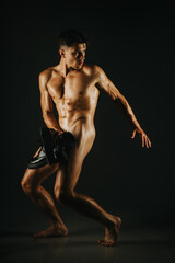 Obraz premium An athletic man displays a dramatic pose in an artistic and dynamic manner. His muscular physique and intense expression convey strength and determination, captured beautifully in soft, dramatic