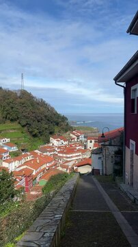 Scenic coastal view in Cudillero, Spain, overlooking the rugged cliffs and turquoise waters of the Cantabrian Sea. The image captures a dramatic landscape framed by lush green vegetation and trees,