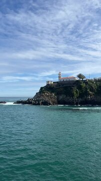 Scenic coastal view in Cudillero, Spain, overlooking the rugged cliffs and turquoise waters of the Cantabrian Sea. The image captures a dramatic landscape framed by lush green vegetation and trees,