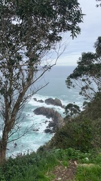 Scenic coastal view in Cudillero, Spain, overlooking the rugged cliffs and turquoise waters of the Cantabrian Sea. The image captures a dramatic landscape framed by lush green vegetation and trees,