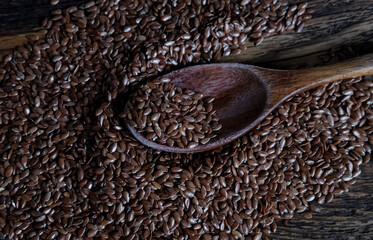 Natural brown flaxseeds in a wooden spoon on a textured wooden surface. Organic superfood for...