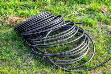 Fototapeta premium A roll of HDPE pipe on the grass in the garden. Installation of drip irrigation for trees and beds