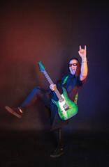 Fototapeta premium Musician rock passionately guitarist plays electric guitar and showing horn gesture against red and blue background