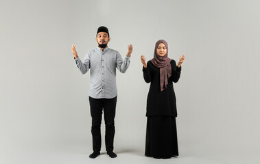 Muslim couple wearing islamic costume praying with open arms, isolated on background studio photo. People religious lifestyle concept_