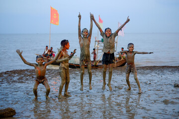 Group of rural children jumping with joy with muddy bodies in a beach near a river 