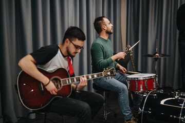 Two musicians collaborating in a recording studio, one playing an acoustic guitar and another on drums, creating a vibrant and creative ambiance.