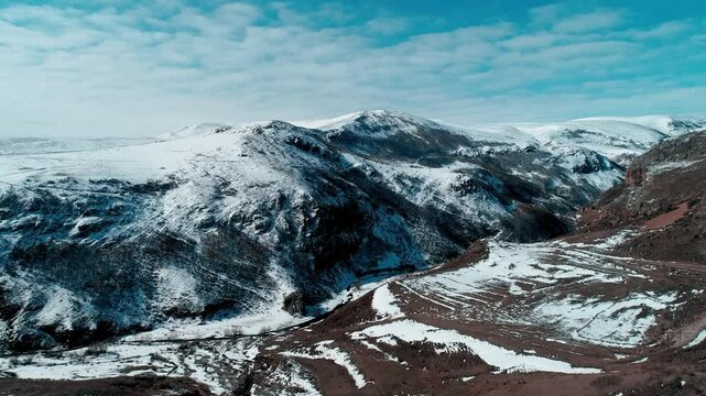 Captured from an aerial view, snow-covered mountains and valleys create a stunning winter landscape. The white peaks and clear blue sky offer a vast and breathtaking view of nature.

