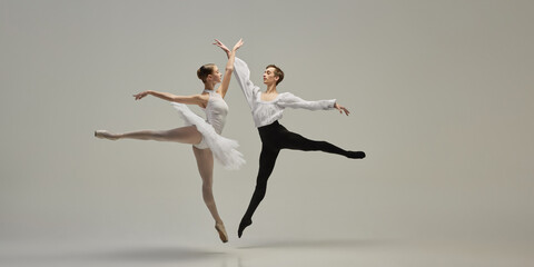Two ballet dancers leaping in perfect synchronization, arms reaching, bodies forming clear lines...