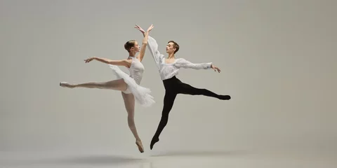 Poster Two ballet dancers leaping in perfect synchronization, arms reaching, bodies forming clear lines against white studio background. Concept of classic dance, freedom, dynamic energy, synergy.