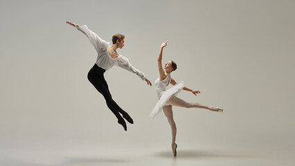 Gravity-defying motion. Ballet duet in poetic airborne movement, arms extended, legs reaching outward against white studio background. Concept of classic dance, passion, energy, rhythm.