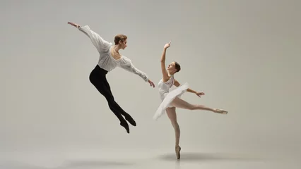 Gravity-defying motion. Ballet duet in poetic airborne movement, arms extended, legs reaching outward against white studio background. Concept of classic dance, passion, energy, rhythm.
