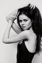 Fototapeta premium Captivating young woman in a black bodysuit, striking a confident pose, showcasing her long hair and expressive emotions against a minimalist light background.