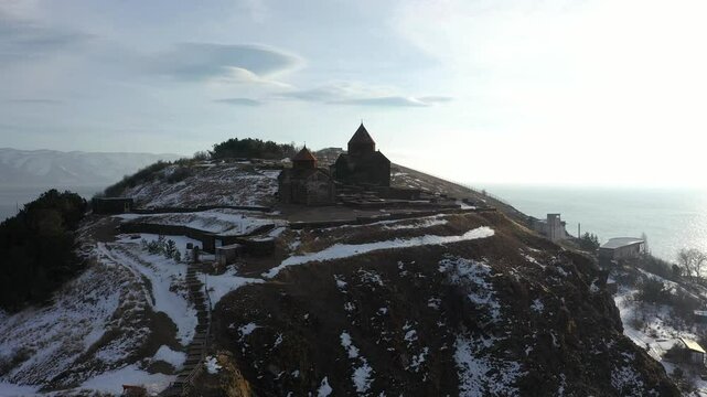 Aerial drone 4K footage of Sevanavank Monastery on Sevan Peninsula during a winter sunrise, overlooking the snow-covered Sevan Lake. The golden light enhances the serene and historic landscape