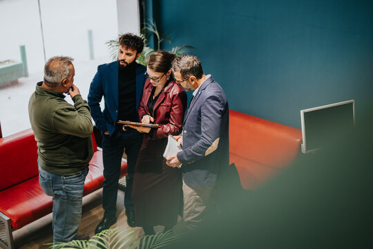 Business colleagues engaged in professional conversation in a corporate office setting, collaborating with documents. The environment showcases teamwork and productivity during a collaborative meeting