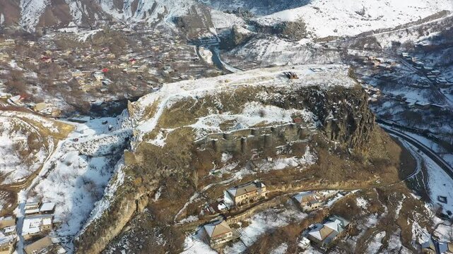 Aerial 4K drone video of a winter view of Bjni village in Kotayk, Armenia, featuring the historic Bjni Fortress, surrounded by snow-covered village houses, winding streets, and the Hrazdan River