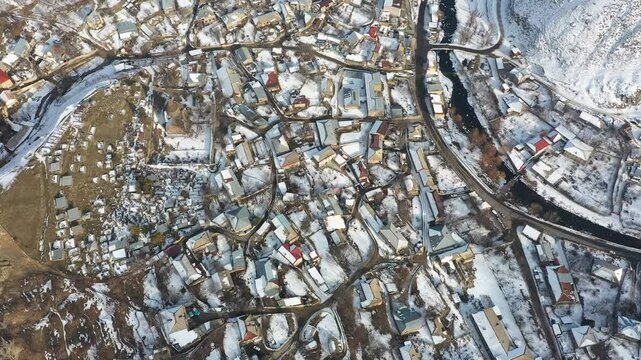 Aerial 4K drone video of winter view of Bjni village in Kotayk, Armenia, featuring historic St. Astvatsatsin church  surrounded by snow-covered village houses, winding streets, and the Hrazdan River