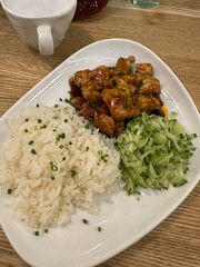 Rice, meat with gravy and fresh cucumbers on plate on wooden background. Vertical. Lunch