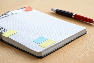 Notebook with sticky notes and a pen on a wooden desk during a brainstorming session