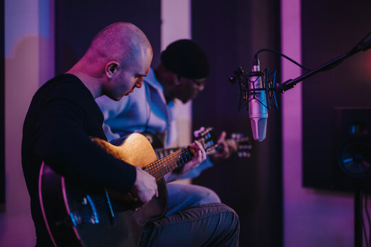 Musicians playing acoustic guitars in a recording studio with purple lighting