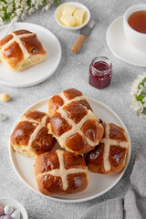 Traditional Easter hot cross buns on a white plate with butter, berry jam and cup of tea. Delicious Easter breakfast.