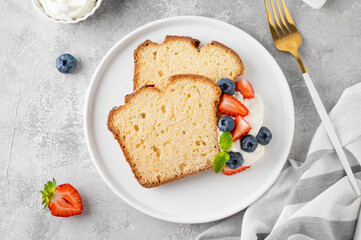 Delicious vanilla pound cake served with fresh berries and whipped cream on a gray concrete background. Selective focus, copy space.