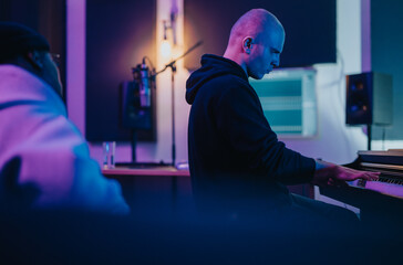 A focused musician plays the keyboard under atmospheric lighting in a modern studio. The setting...