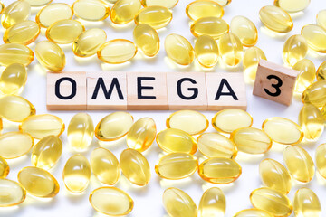 Close-up of yellow capsules of Omega-3 fatty acid supplement scattered on a light table. In the...