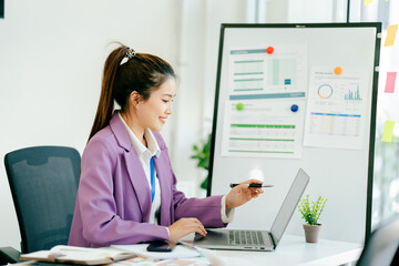 Woman in a purple jacket is sitting at a desk with a laptop
