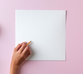 Female hand about to write on a blank sheet of paper on a pink surface in a creative workspace
