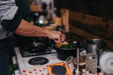 A person is preparing a hot meal in a cozy kitchen with fresh greens. The surroundings are equipped with traditional cooking utensils and cutlery, creating a warm and inviting atmosphere.