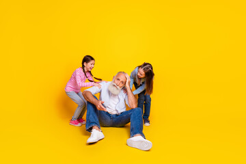 Grandfather Sitting on a Yellow Background with Two Playful Granddaughters