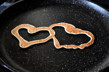 A pancake in the form of two joined hearts on a black spotted pan. selective focus. Maslenitsa holiday. curly pancakes