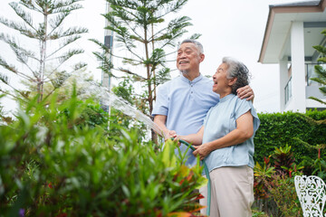 Senior man and woman are happily watering their garden with a hose. They share smiles and laughter...