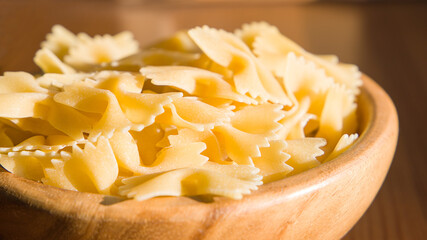 Farfalle pasta in a wooden bowl on a wooden table. Selective focus.