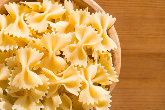 Farfalle pasta in a wooden bowl on a wooden background. Top view.