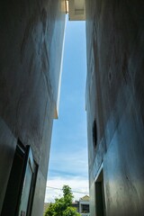 Narrow alleyway between tall modern buildings with a clear blue sky above. Urban architecture perspective with light and shadow contrast. Cityscape view from a low angle.