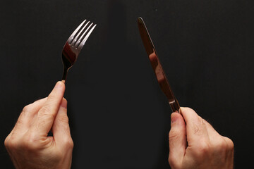 Knife and fork in hands on a black background