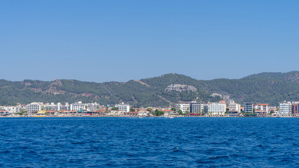 Fototapeta premium View from Mediterranean Sea on houses and hotels of city of Marmaris, Turkey on background of green hills and mountains