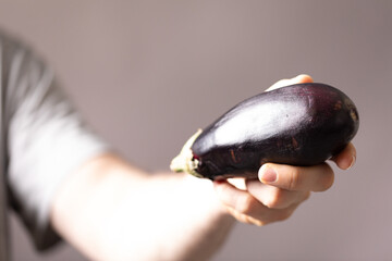 Close-up of a hand holding a ripe eggplant against a muted background.