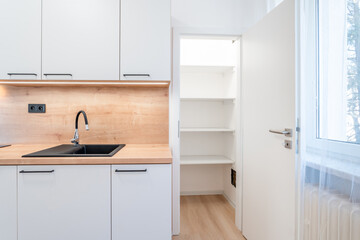 Modern white kitchen with open pantry door showing empty shelves and sink